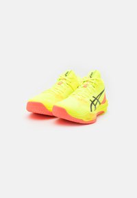 Zapatillas deportivas de color amarillo brillante con parte superior de malla texturizada, rayas laterales negras, acentos rosas en la suela y cordones para un ajuste seguro.