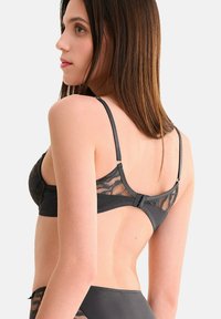 Zwarte kant beha met gaasdetails, verstelbare banden en een haaksluiting op de rug, voorzien van een gladde stof en een ingewikkeld patroon.