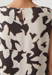 Gros plan sur un haut sans manches avec un motif floral abstrait noir et blanc et une petite fermeture à bouton en forme de trou de serrure à l'arrière de l'encolure.