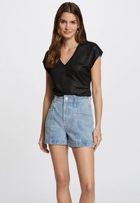 Zwart T-shirt met korte mouwen en een V-hals, afgewerkt met zilveren randen, gecombineerd met lichtblauwe denimshorts met voorzakken en een riemlus.