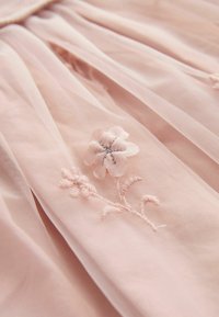 Rosa tylltyg med delikat blommönster med en ljusrosa blomma och intrikata stålkanter. Mjuk, genomskinlig textur.