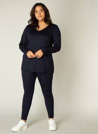Donkerblauwe langarmtop met V-hals en bijpassende leggings; gemaakt van soepel stretchmateriaal; gecombineerd met witte sneakers.