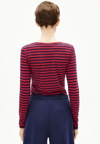 Langärmliges gestreiftes Oberteil in Marineblau und Rot, mit einem runden Halsausschnitt und taillierter Passform. Kombiniert mit Marineblauen Hosen mit einer Gesäßtasche.