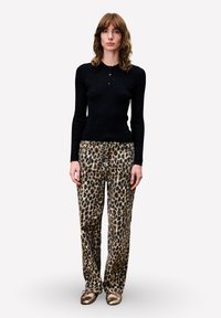 Zwarte geribbelde langemouwen top met kraag, gecombineerd met losse broek met luipaardprint. Model draagt metallic gouden ballet flats.