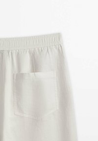 Pantalons en lin beige clair avec une taille élastique, dotés d'une poche arrière unique et d'une finition en tissu texturé.