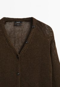 Cardigan en tricot marron fabriqué en 100 % lin, avec un col en V, de grands boutons noirs et une texture de tricot lâche et ouverte.