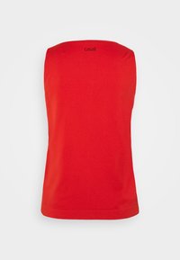 Haut de sport rouge sans manches avec une texture chevron subtile et un petit logo noir « casall » près de l'encolure sur fond blanc.