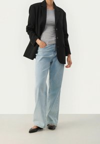 Zwarte op maat gemaakte blazer over een grijs aansluitend T-shirt, gecombineerd met lichtblauwe wijde jeans en zwarte puntige flats.