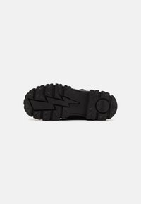 Semelle en caoutchouc noir d'une chaussure robuste, avec des motifs de crampons profonds, un design en zigzag et une surface texturée pour une meilleure adhérence et durabilité.