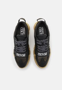 Zapatillas Versace Jeans Couture en negro y marrón con cordones estampados, detalles de malla y una correa con la marca en la parte superior, vistas desde arriba.