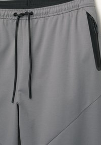 Grå atletiske shorts med et tekstureret stof, elastisk talje, sort snøre og en lynlåslomme på siden.