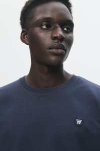 Navy blue cotton t-shirt with a crew neckline and a circular embroidered logo on the chest. Soft texture, minimalistic design.