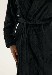 Czarny pluszowy szlafrok z pikowanym wzorem w romby, przewiązywany w talii, z długimi rękawami. Miękka tekstura o gładkim wykończeniu.