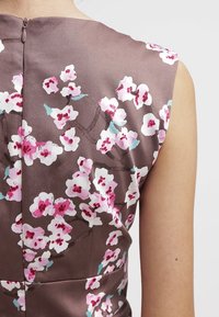 Brun satin kjole med pink og hvid blomster mønster, med rund halsudskæring og ærmeløs design, lynlås lukning bagpå.