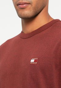 Μαρόν μπλούζα τύπου crew neck φτιαγμένη από βαμβάκι με απαλή υφή. Διαθέτει ένα μικρό λευκό ορθογώνιο λογότυπο στο στήθος με την ένδειξη "TOMMY JEANS".