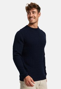 Mørkeblå kabelstrikket genser med ribbet rund hals og lange ermer, laget av et teksturert stoff, med en tettsittende silhuett.