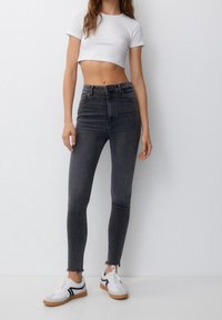 Vaqueros negros de cintura alta con un corte ajustado, bajo deshilachado y diseño de stretch ceñido. Combinados con una blusa blanca corta y zapatillas deportivas.