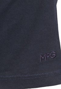 Marineblauwe katoenen stof met ribbelstructuur; voorzien van een gestikt "M'oG"-logo in paars aan de onderrand en een eenvoudig, gestructureerd ontwerp.