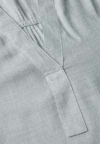 Gros plan sur un tissu gris clair avec un tissage en toile diagonale et des coutures superposées formant une forme en V.