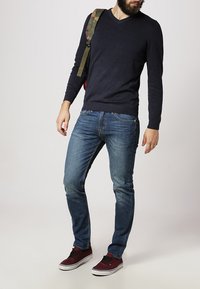 Dark blue v-neck sweater, light blue jeans, and burgundy sneakers. The outfit is complemented by a camouflage backpack.