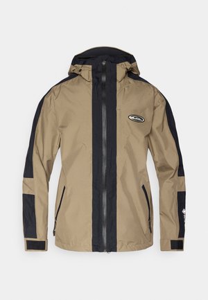 Ūdensnecaurlaidīga jaka khaki un tumši zils, ar pilnu rāvējslēdzēju, regulējamu kapuci un logotipu. Aprīkota ar kabatām ar rāvējslēdzēju un Velcro aprocēm. Klasiska piegriezuma.