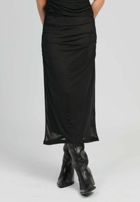 Jupe noire, longueur genou, en tissu doux et lisse, avec des détails froncés et une silhouette ajustée, associée à des bottes noires sculpturales montantes.