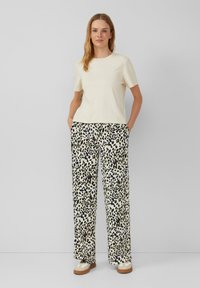 Cremfarbendes T-Shirt mit Rundhalsausschnitt, kombiniert mit lockeren, beigen und schwarzen leopardgemusterten Hosen, die seitliche Taschen und eine entspannte Silhouette aufweisen.