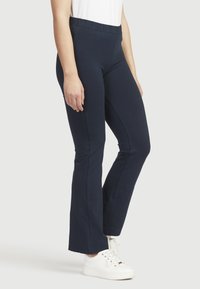 Marineblaue Schlaghose aus einem weichen, dehnbaren Stoff. Mit einem elastischen Bund und einer glatten Textur. Getragen mit weißen Sneakers.