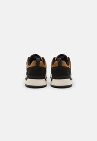 Bruna och svarta sportskor med överdel i mocka, strukturerad tyg och en beige mellansula. Har förstärkt häl och snörningsdesign.