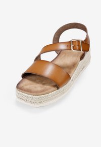 Sandalia de cuero marrón con dos correas anchas, plantilla texturizada, correa para el tobillo tipo corcho y suela de plataforma envuelta en yute. Hebilla de metal ajustable.