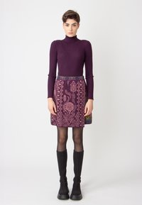 Purple ribbed turtleneck paired with a patterned skirt featuring floral designs in pink on a dark background. Black knee-high boots.