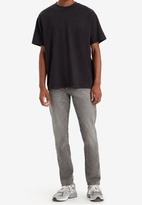 T-shirt de algodón negro con mangas cortas y cuello redondo, combinado con jeans gris claros y zapatillas grises, con un sutil logo en el pecho.