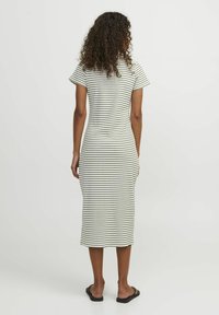Robe midi rayée en beige clair et noir. Manches courtes, design ajusté, texture côtelée et fentes latérales. Des sandales plates complètent le look.