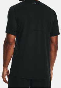 Hombre vestido con una camiseta atlética negra de manga corta sin estampados, con un pequeño logo de Under Armour en la parte superior de la espalda.