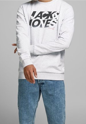 Sudadera gris con gráfico negro "JACK & JONES" en la parte frontal. Puños y dobladillo acanalados, textura suave, combinada con jeans de mezclilla azul.