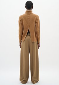 Brun ribstrikket rullekravesweater med slids bagpå, kombineret med brede beige bukser med bælte og plissé detaljer.