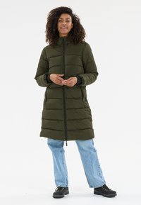 Lang, olivengrøn, polstret frakke med højt krave, lynlås og to sidelommer. Modellen bærer lyseblå jeans og sorte støvler.