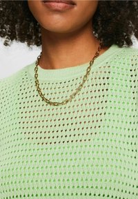 Jasnozielony, dziergany sweter z otwartym wzorem siateczkowym. Na górze znajduje się złoty łańcuszek z ogniwami, który dodaje metalicznego akcentu.