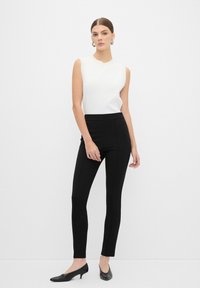 Haut sans manches blanc associé à un pantalon noir taille haute et des ballerines noires. Design simple, texture lisse et silhouette ajustée.