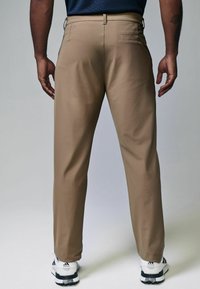 Khakihosen mit geradem Schnitt, ausgestattet mit einer glatten Textur, Gesäßtasche und Gürtelschlaufen, kombiniert mit weißen und schwarzen Sportschuhen.