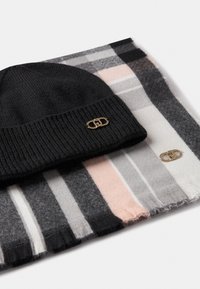 Czarna dzianinowa czapka z widocznym fasonem i złotym wykończeniem, w połączeniu z szalikiem w kratę w czarne, szare, białe i różowe paski.