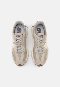 Par beige og lysebrune New Balance-sneakers med snørebånd, set oppefra på en hvid baggrund.