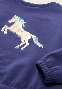 Felpa blu navy con un design di unicorno bianco realizzato in paillettes, con una criniera testurizzata in blu e accenti metallici.