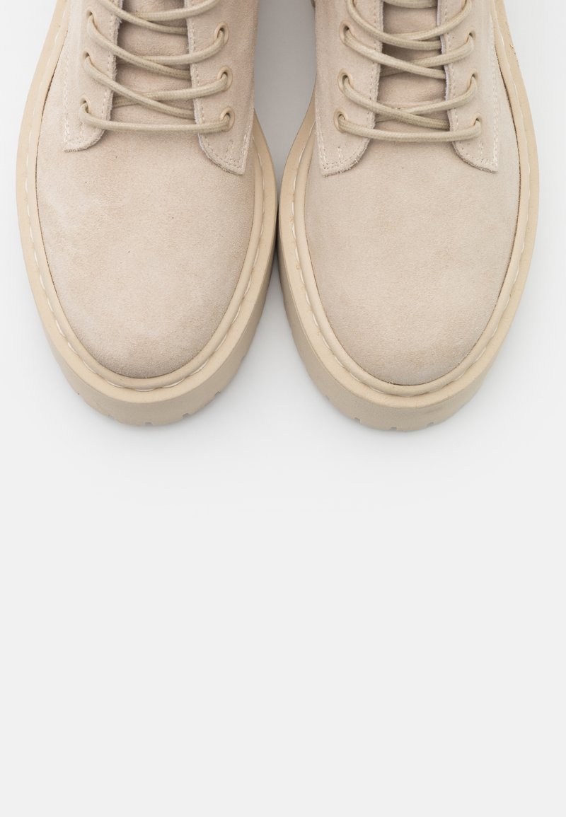 Stivaletti alla caviglia in suede beige con punta rotonda, dotati di lacci abbinati e suola in gomma cremisi spessa. Texture liscia con dettagli di cucitura minimal.