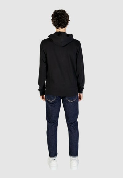 Felpa nera con cappuccio e vestibilità rilassata, abbinata a jeans blu scuro. Il tessuto appare liscio e l'aspetto complessivo è casual.