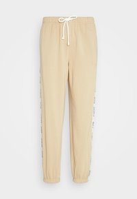 Beige sweatpants with an elastic waistband, drawstring, and cuffed hems. Features contrasting white side stripes with printed text.