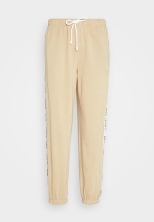 Beežid dressipüksid elastse vöökoha, paelaga ja mansettidega. Omavad kontrastset valget külgistrippi, millel on trükitud tekst.