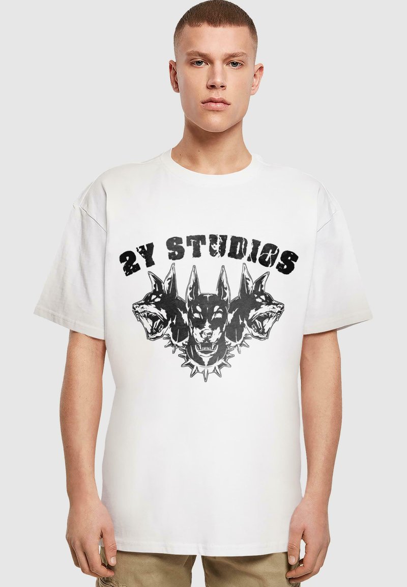 Fehér, rövid ujjú póló, fekete grafikával, három kutyafej látható rajta, tüskés gallérral, felette pedig a kiemelkedő "2Y STUDIOS" felirat.