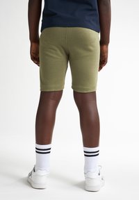 Shorts en coton vert olive, ajustés, longueur mi-cuisse, avec ceinture côtelée et élastique, associés à des chaussettes blanches et des baskets.