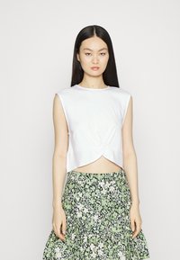 Top branco curto com um design torcido na frente, apresentando um decote redondo e sem mangas, combinado com uma saia verde floral.